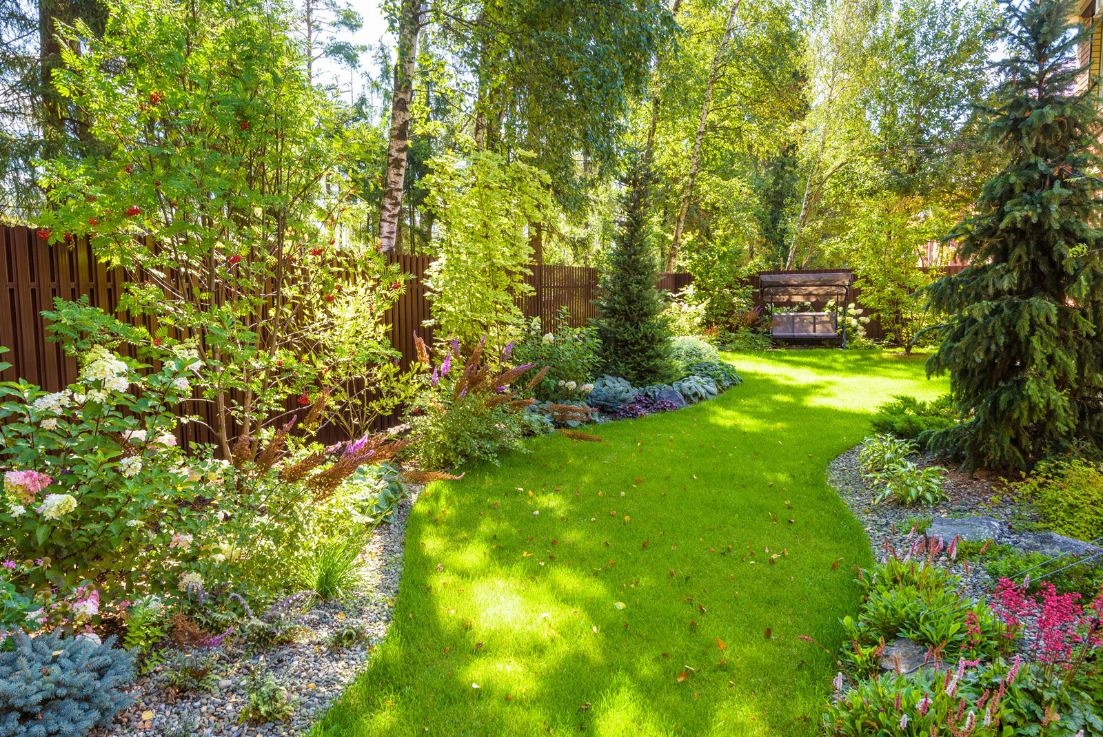 Garden with a winding green grass pathway and native trees and shrubs on the right and left side of the path